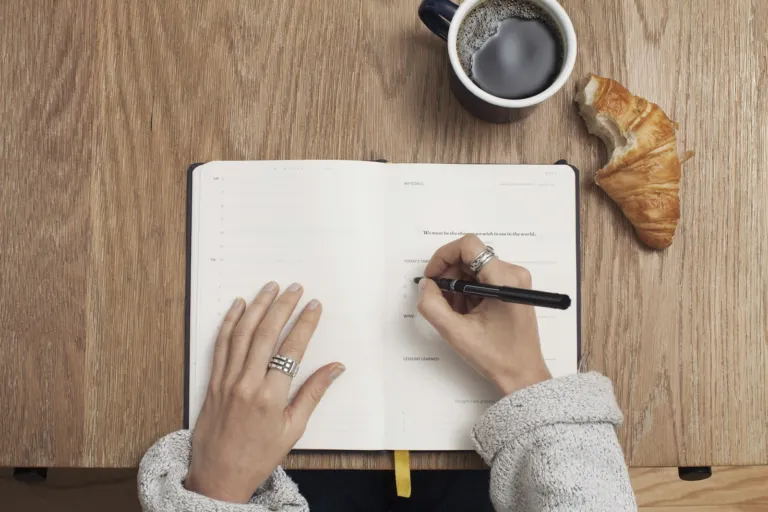 Hands writing notes in a journal next to coffee, representing the Songoftruth.org editorial process