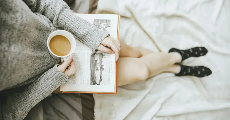 Person relaxing with a book and a cup of coffee on a cosy bed